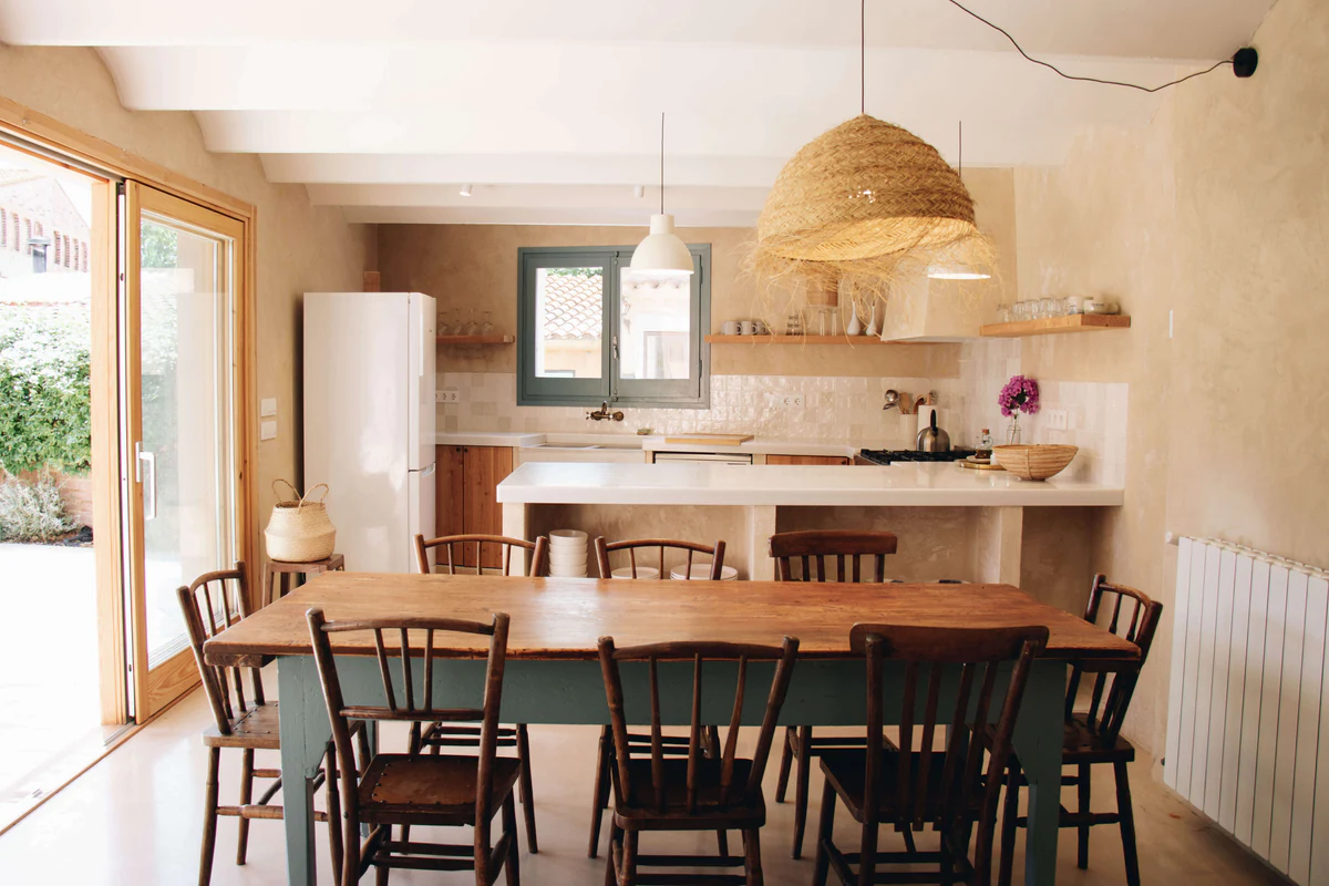 Cocina con lámparas colgantes blancas y una pantalla de fibras naturales sobre la mesa