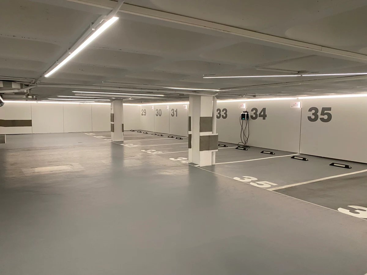 Planta del aparcamiento con luminarias lineales y la numeración de las plazas en la pared