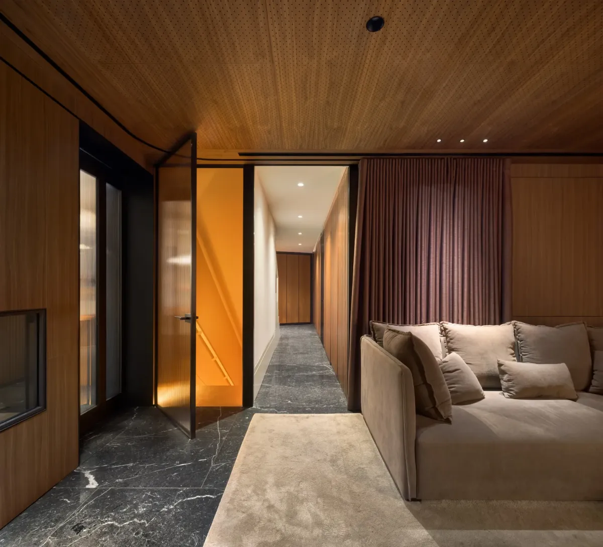 Pasillo de una vivienda en Barcelona con techo de madera, luz indirecta y escalera iluminada al fondo